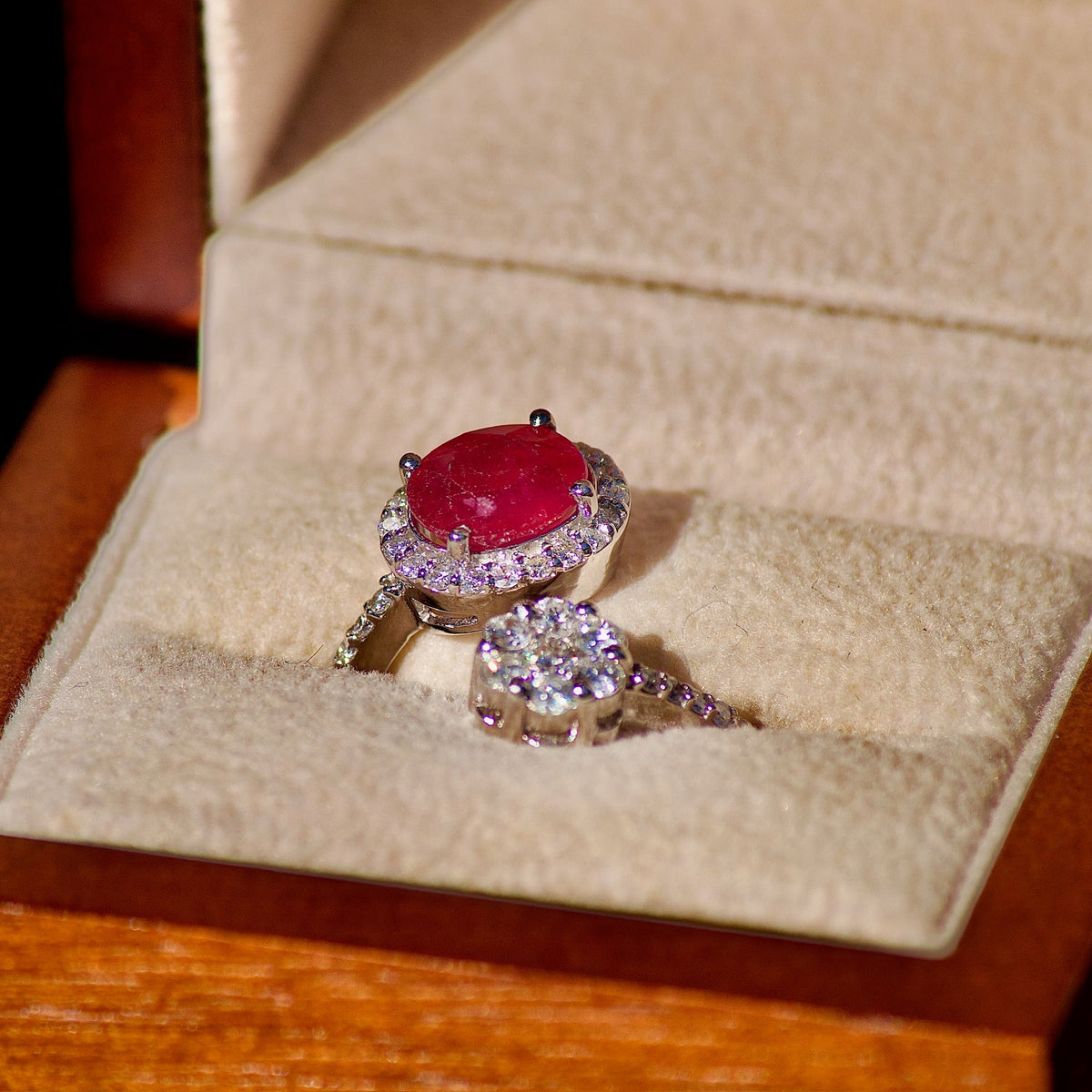 Ruby halo ring in a ring box beside a white stone cluster ring