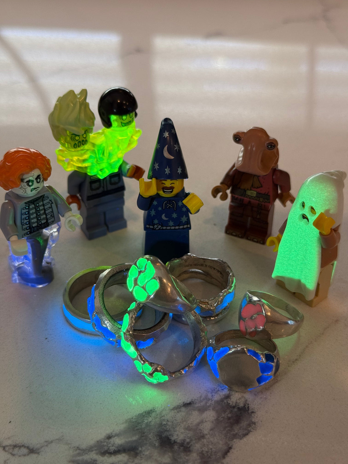 Rings with green and blue glow enamel, glowing next to toy figures